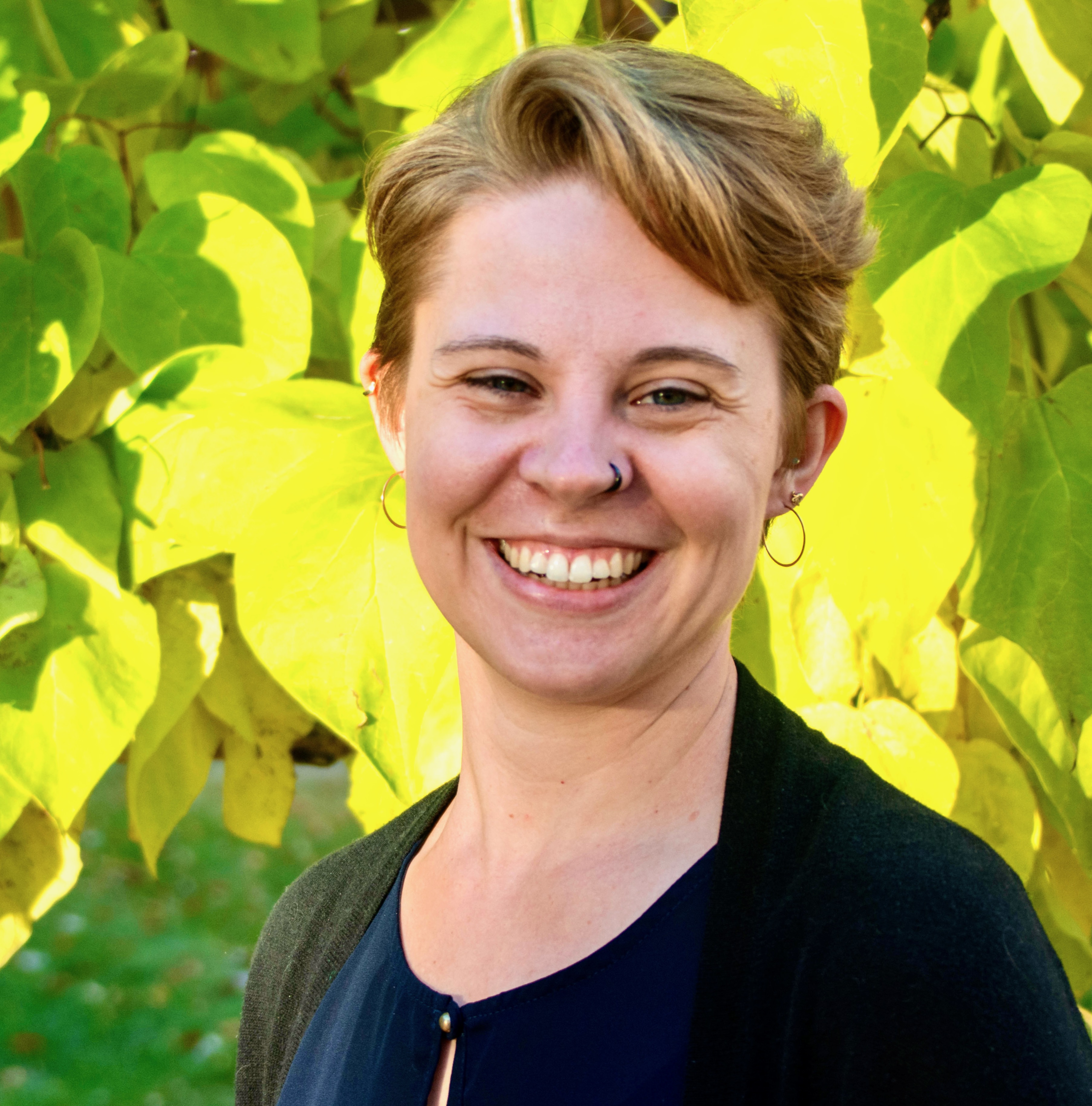 A picture of Jessie standing in front of green leaves.